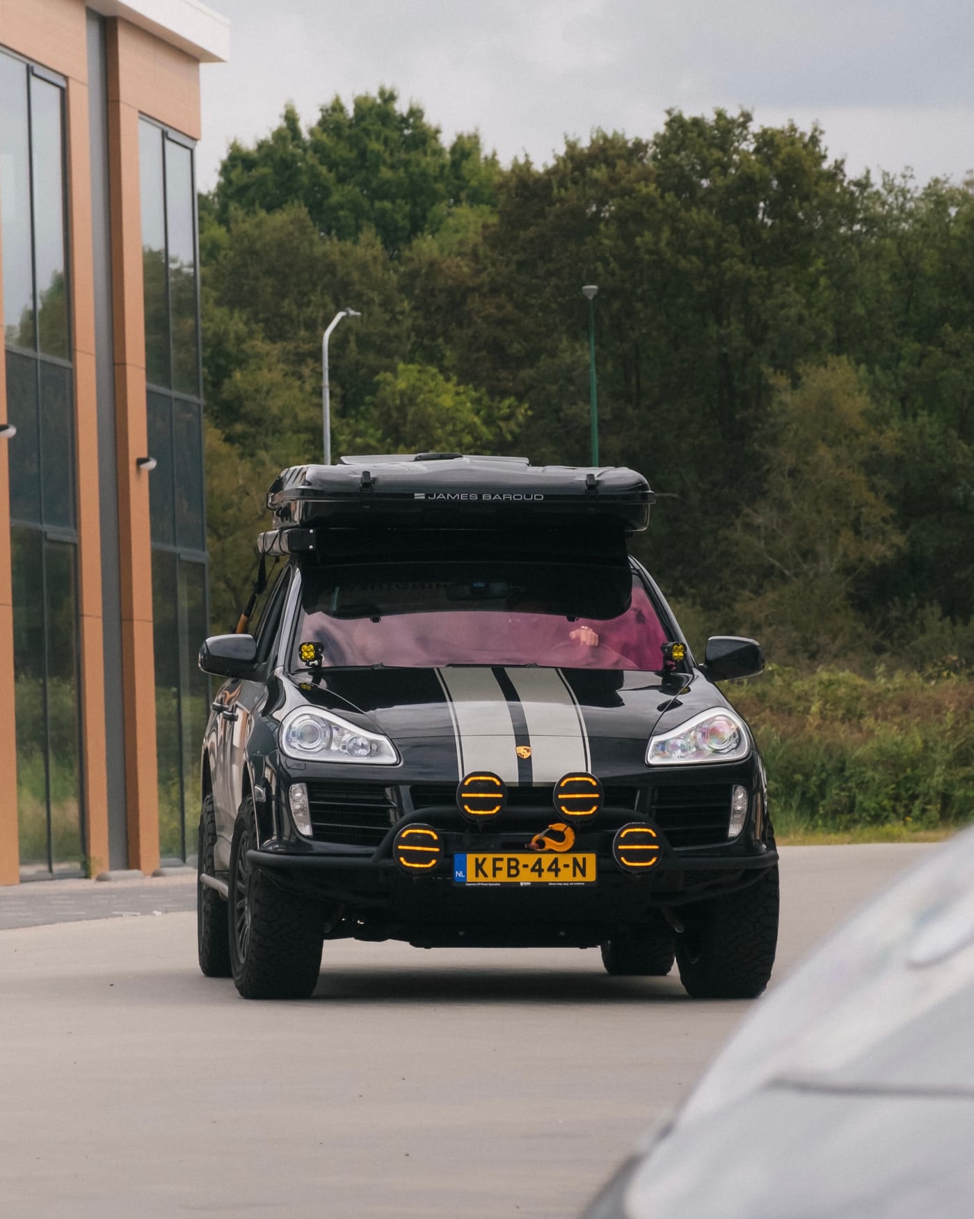 Our black Cayenne driving towards the camera: James Baroud roof tent, silver stripes over the bonnet, yellow spotlights and a winch on the steel bumper