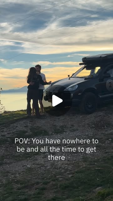 Tess and Bodhi hugging next to the Cayenne above a lake at sunset: "POV: You have nowhere to be and all the time to get there"
