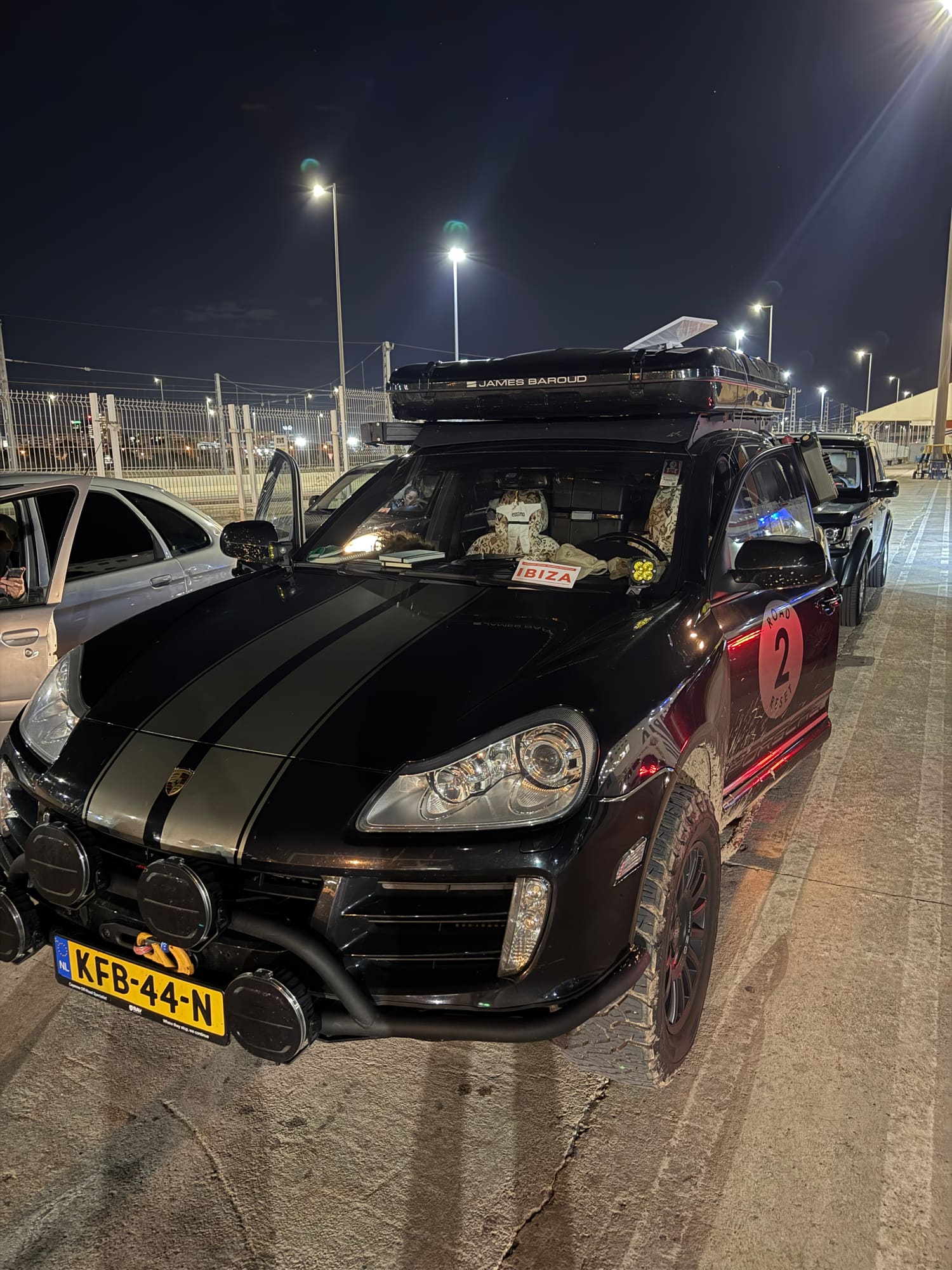 The Cayenne at night in the ferry queue in the port of Valencia, roof tent closed and an "Ibiza" sign behind the windscreen