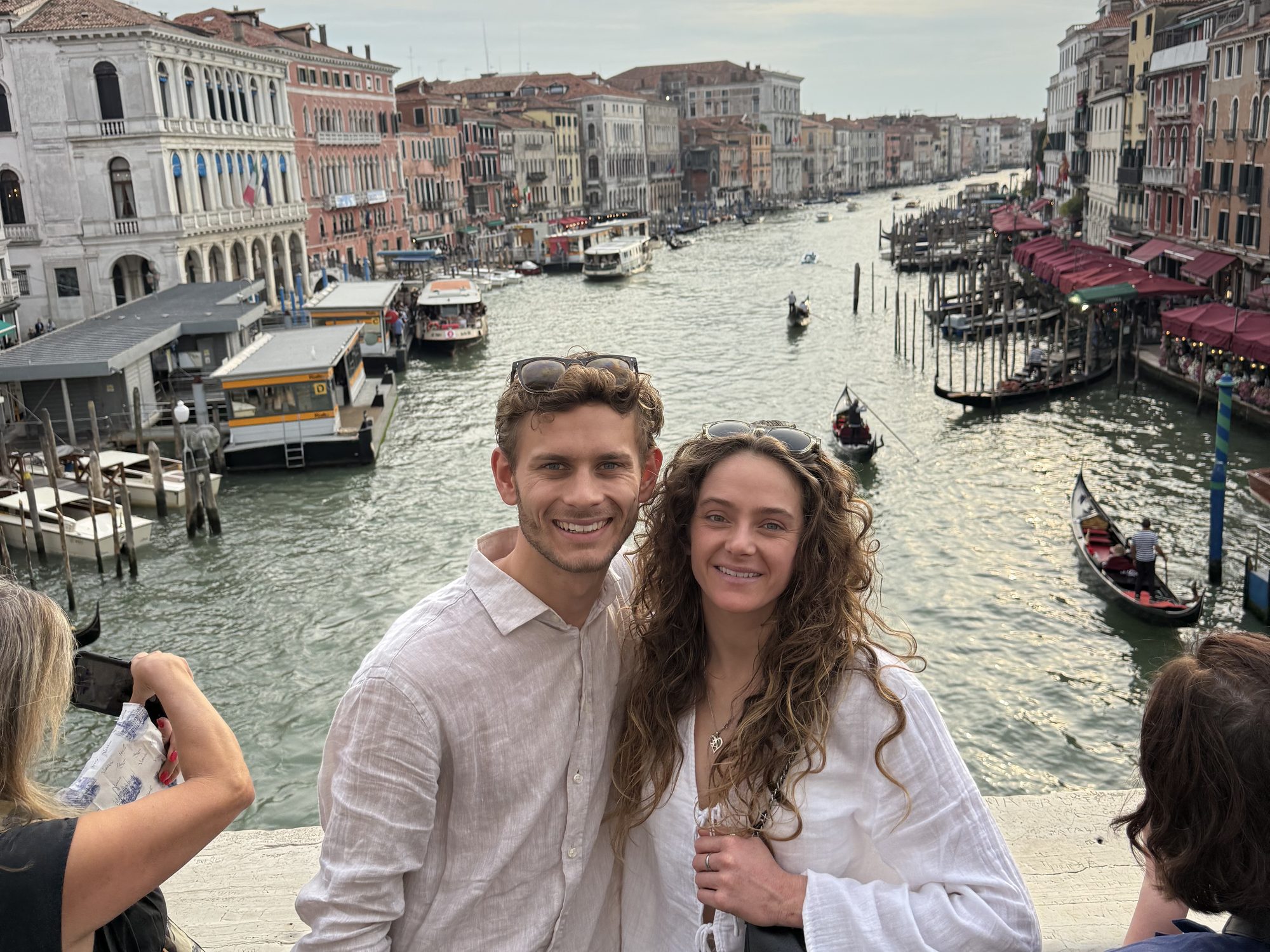 Bodhi and Tess smiling on the Rialto Bridge, with gondolas on the Grand Canal behind them