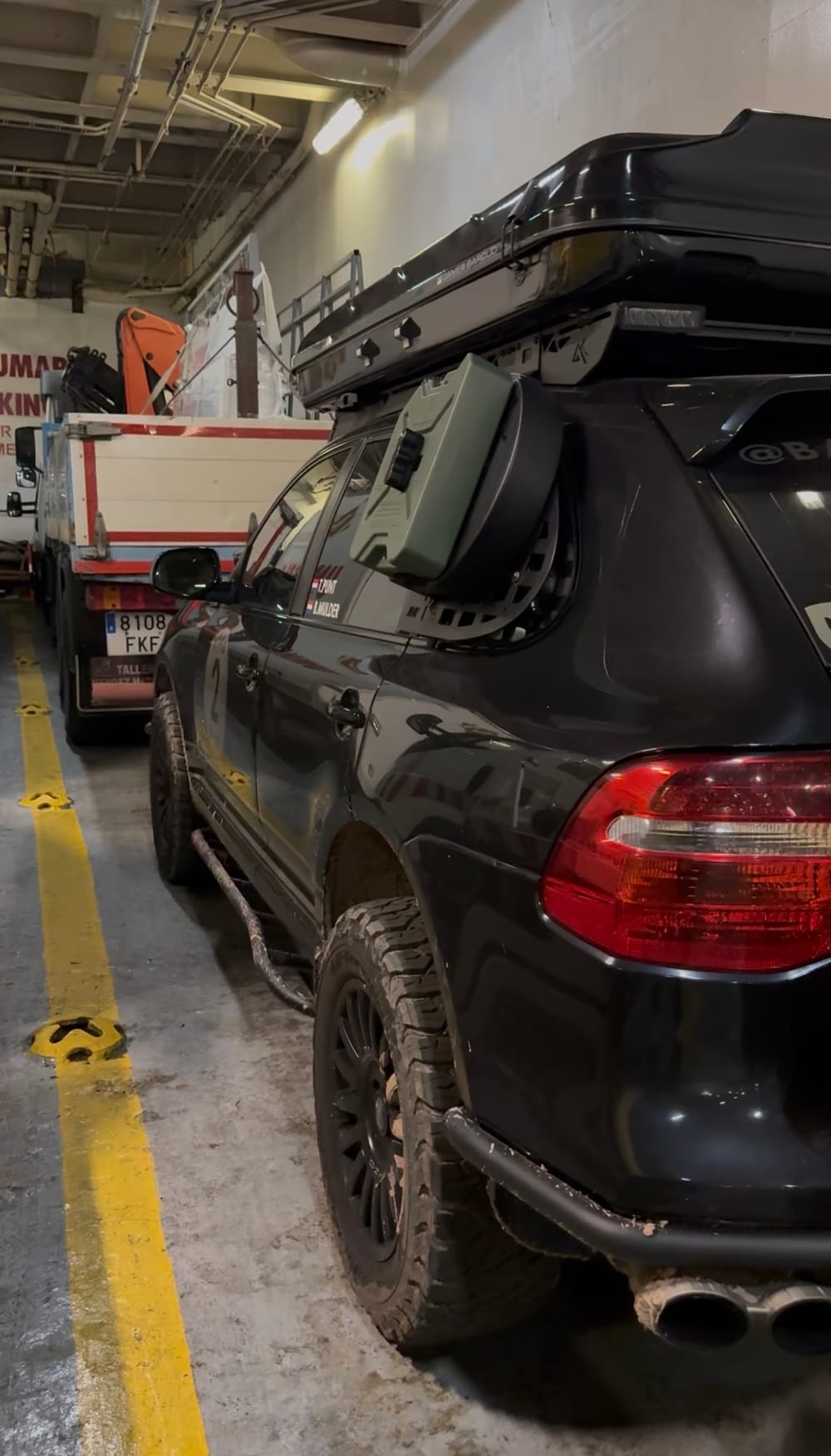 The Cayenne parked on the ferry's car deck behind a lorry with a crane, jerry can on the side and mud on the tyres